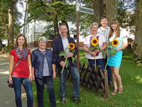 Mit Sonnenblumen im Gepäck nach Sonnenschein: Kreisdirektor Jochen Hagt (3. von links) mit Anwohnern unter dem passenden Straßenschild. (Foto: OBK)