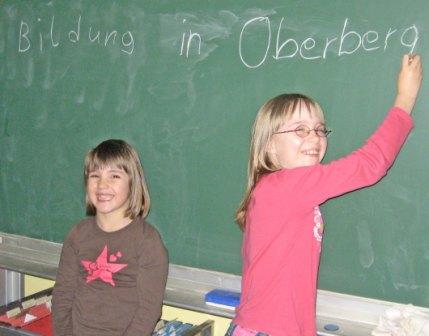 Das Foto zeigt eine schreibende Schülerin - Schriftzug: Bildung in Oberberg - und eine lachende Schülerin vor einer Schultafel. (Foto: OBK) 