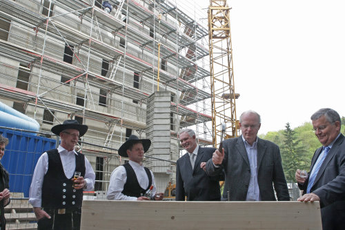 Der Berufskollegleiter Wolfgang Saupp bearbeitet den letzten Balken für den Neubau, unterstützt vom leitenden Kreisbaudirektor Uwe Stranz und Landrat Hagen Jobi (Foto: OBK)