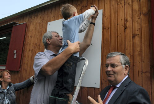 Der fünfjährige Christian Thiel brachte gemeinsam mit Landrat Hagen Jobi und Bürgermeister Hilko Redenius, das Schild mit dem Logo des Oberbergischen Kreises am Aufenthaltswagen an. (Foto: OBK)