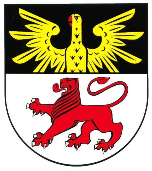 Wappen mit schwarzem Schildhaupt, darauf ein gelber Adler mit roten Details. Darunter ein weißes Feld mit einem roten, schreitenden Löwen mit schwarzer Mähne.