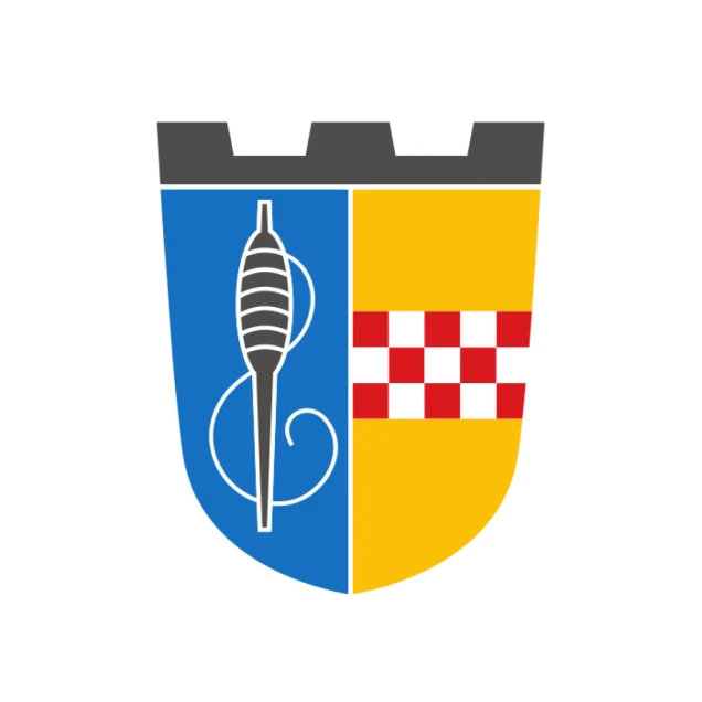 Ein Wappen mit einer grauen Zinnenkrone oben. Das Schild ist vertikal zweigeteilt: links blau mit einer Spindel, rechts gelb mit einem rot-weißen Schachbrettmuster.