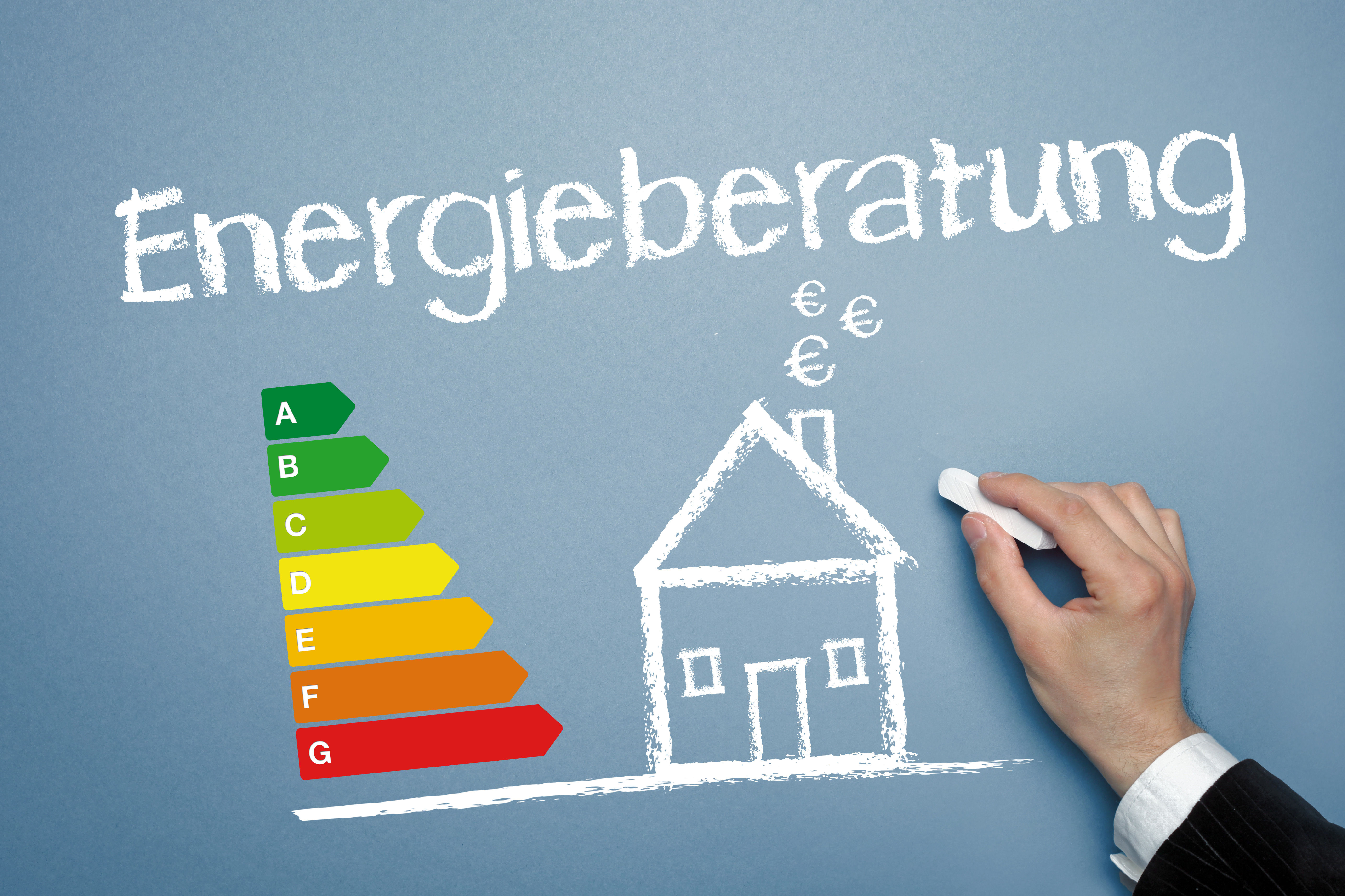 Eine Hand zeichnet mit Kreide ein Haus auf eine blaue Tafel. Links ist eine Energieeffizienzskala von A bis G dargestellt. Darüber steht das Wort 'Energieberatung'.
