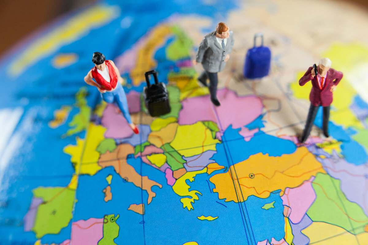 Miniaturfiguren von Reisenden stehen auf einer Karte Europas. Die Figuren sind mit Koffern ausgestattet und in verschiedenen Farben gekleidet.
