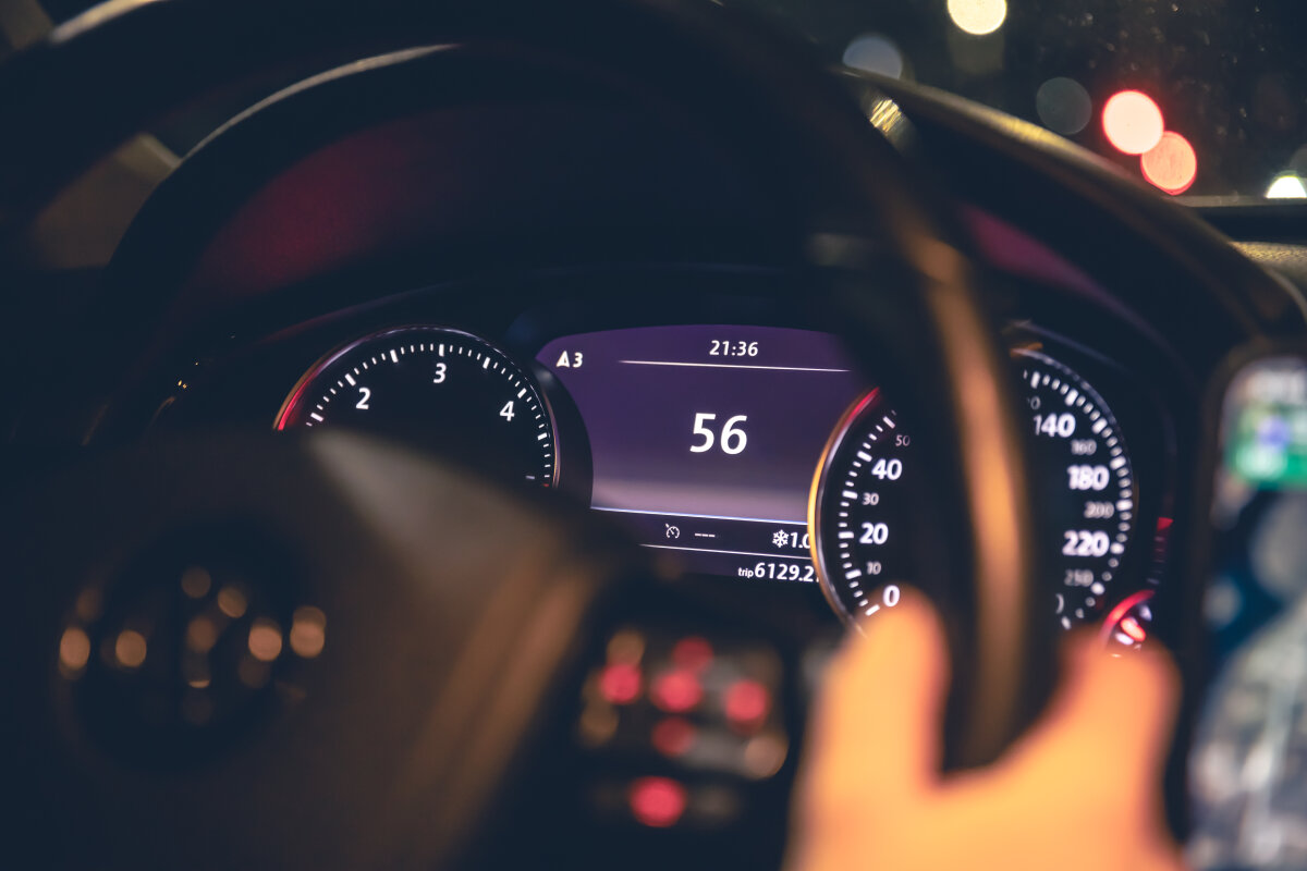 Nahaufnahme eines beleuchteten Fahrzeugcockpits bei Nacht. Zu sehen sind ein Lenkrad, Instrumententafeln mit Tachometer und Drehzahlmesser sowie digitale Anzeigen.