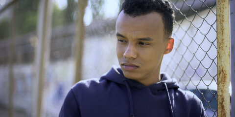 Young refugee from dysfunctional family leaning on fence, orphan teenager