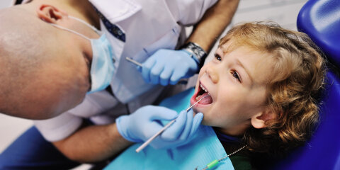 Male dentist examines the teeth of the patient cheerful child with curly red hair. Moloi boy smiling in dentist's chair. child mouth wide open in the dentist's chair