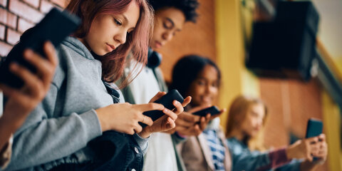 Group of teenagers using mobile phones in hallway at high school.