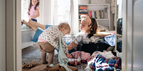 Tired mother with small toddler daughter in messy bedroom at home, resting.