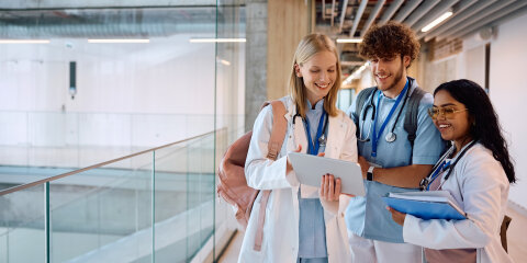 Group of happy medical and nursing students using digital tablet in hallway.