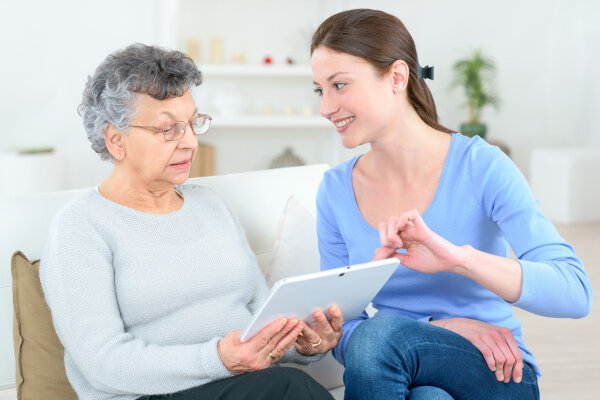 young lady helping elderly woman use a digital tablet