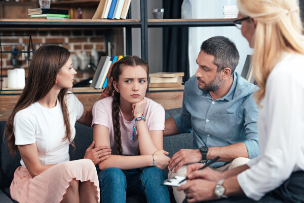 parents cheering up daughter on therapy session by female counselor in office