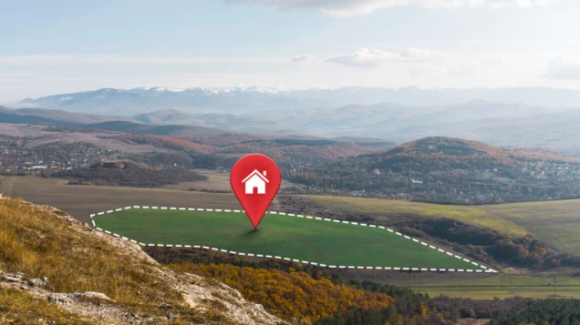 Weitläufige Landschaft mit Hügeln, Bäumen und Wiesen. Ein Grundstück ist mit gestrichelten Linien markiert, darauf ein roter Standort-Pin mit Haus-Symbol.