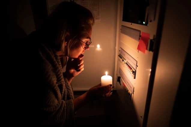 A girl is checking an electrical shield after an electrical blackout. Using a candle in the dark trying to figure out what happened. Electrical malfunction.