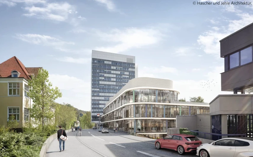 Städtische Straßenszene mit modernen und historischen Gebäuden. Im Vordergrund parken Autos, eine Person geht auf dem Gehweg, und im Hintergrund ist ein hoher Bürokomplex zu sehen.